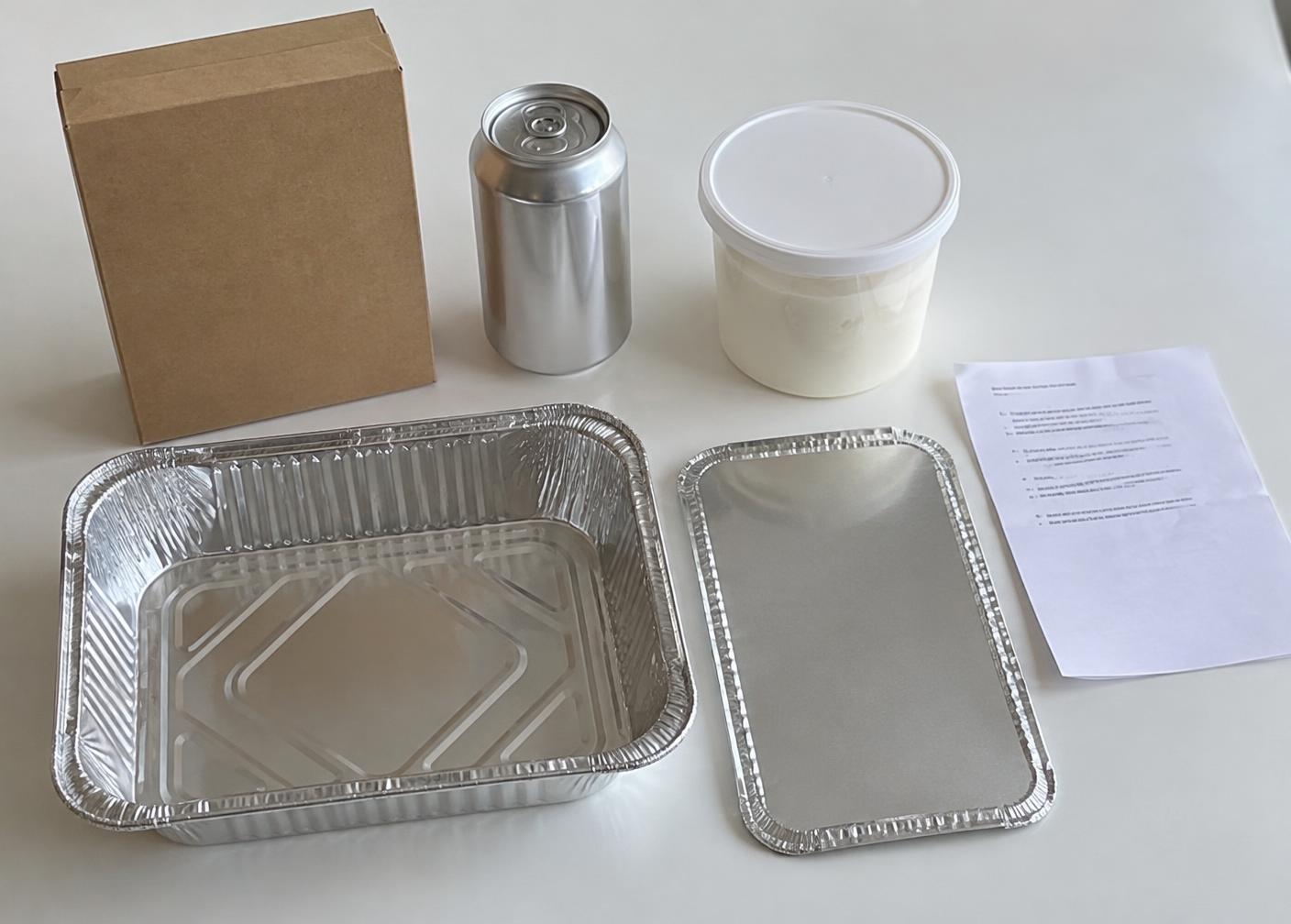 Kit contents on a white table: a cake mix box, a soda can, a frosting tub, an aluminum pan with lid, and an instruction sheet